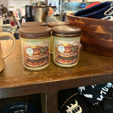 Two candles labeled 'Pineapple Breakfast' on a wooden counter with a blurred cafe background.