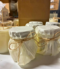 Jars wrapped in plastic and tied with twine on a white surface, with cardboard boxes in the background.